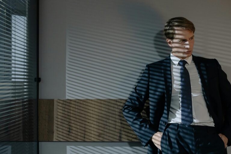Businessman in suit, relaxed in office with dynamic shadow patterns from window blinds.
